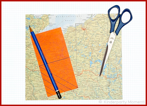 auf einer Landkarte liegt eine orange Lesezeichenvorlage, ein Bleistigt und eine Schere