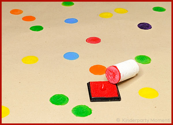 Korken auf rotem Stempelkissen auf einem Bogen Packpapier mit bunten Stempelpunkten
