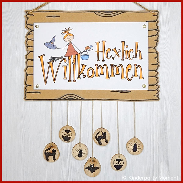 Türschild mit ausgemaltem Bild von kleiner Hexe, daran hängen Ketten mit kleinen Holzscheiben