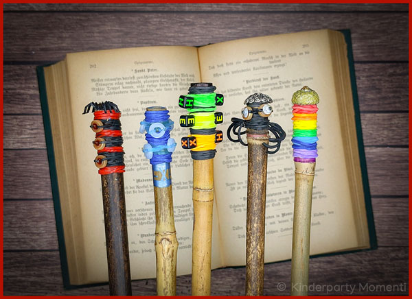 fünf Zauberstäbe mit Loom Gummis umwickelt vor einem alten Buch