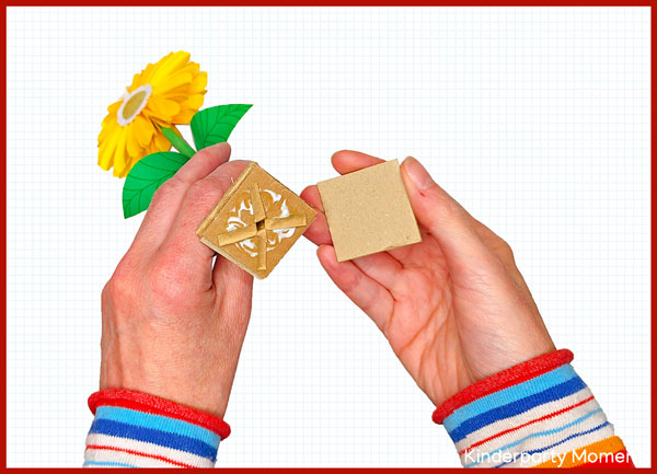 Hände halten eine gelbe Papierblume mit Pappfuß