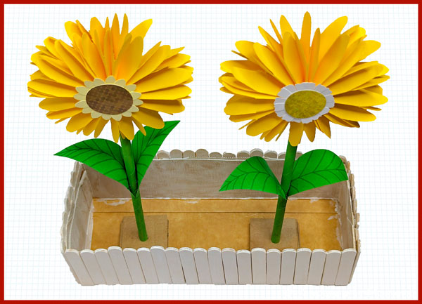 in einem Blumenkasten aus Holzstäbchen stehen zwei Sonnenblumen aus Papier