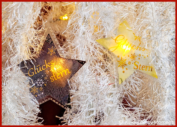 zwei leuchtende Sterne einer selbstgebastelten Lichterkette in einem aus weißer Wolle gehäkeltem Tannenbaum